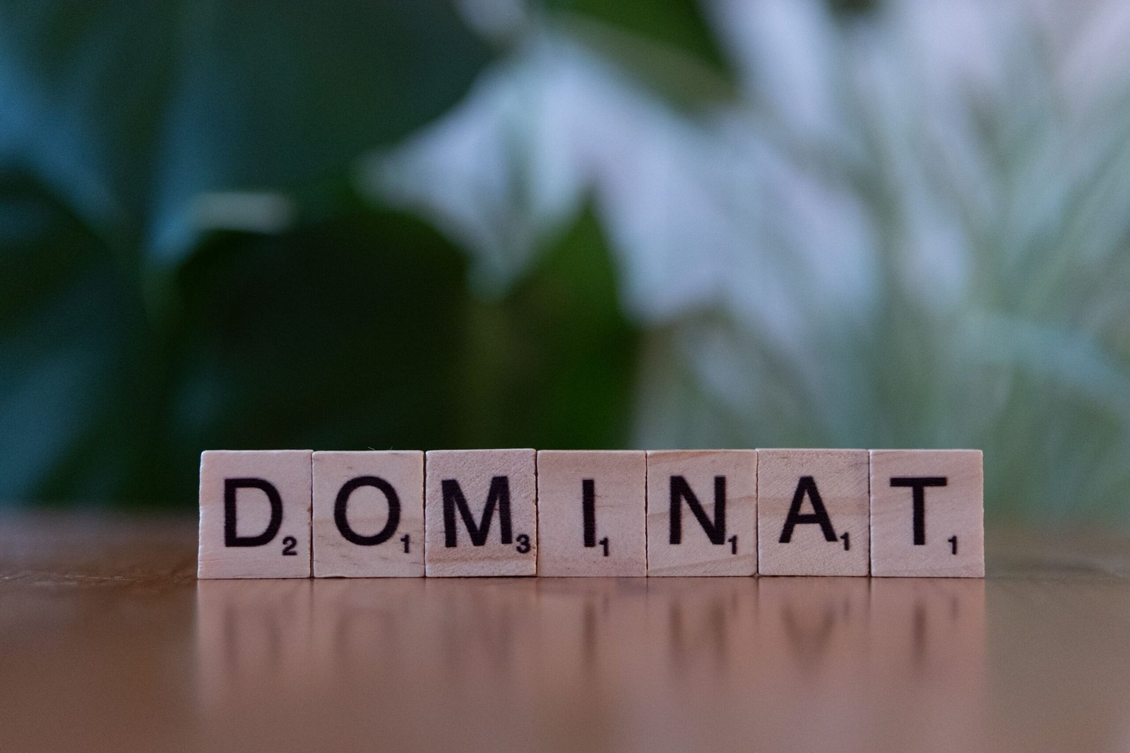 Scrabble tiles spelling 'DOMINAT' on a wooden surface with blurred background.